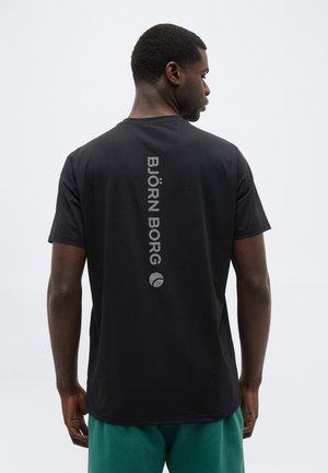 Mężczyzna pokazany od tyłu, ubrany w czarną koszulkę z krótkim rękawem z pionowym napisem i logo "BJÖRN BORG" na środku pleców.