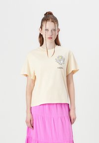 Light yellow cotton t-shirt featuring a graphic design of a flower and doodle. Paired with a pink tiered skirt. Simple, relaxed fit.