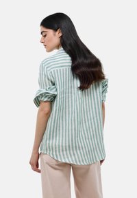 Chemise à manches longues rayée vert clair et blanche en tissu doux. Comprend des poignets retroussés et un ourlet incurvé à l'arrière.