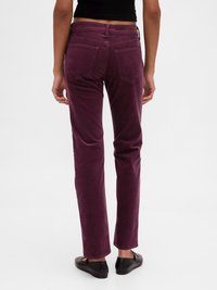 Pantalon droit en velours côtelé violet avec poches arrière, taille moyenne et texture douce. Des chaussures plates sont portées avec le pantalon.