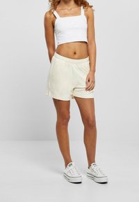 Vit kortärmad linne med fyrkantig ringning, kombinerad med ljusbeige shorts med elastisk midja och fickor, komplett med vita sneakers.