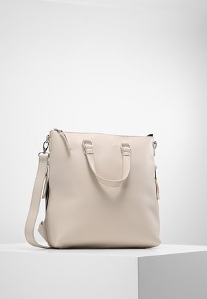 Sac à main en cuir beige avec deux poignées et une bandoulière amovible, présenté sur un piédestal blanc sur un fond clair.