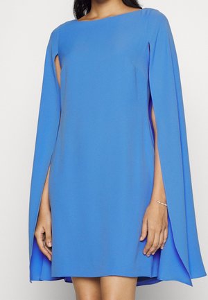 Robe bleue avec un encolure droite, courte, et des manches en cape. Tissu lisse, design minimaliste, et détails de découpes sur les côtés.