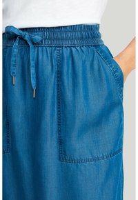 Blå snøre-skirt med en sammensamlet talje, to sidelommer og subtile stikninger på stoffet for tekstur.