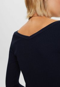 Sini sinirikkäissä pitkähihaisissa paidoissa on V-muotoinen kaula-aukko, joka on valmistettu tekstuuripinnasta ja istuvasta siluetista. Korostukset sisältävät näkyvää ompelua.