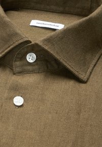Col de chemise en lin marron et boutons supérieurs avec une étiquette blanche affichant le nom de la marque « seidensticker ».
