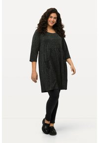 Robe tunique noire texturée à manches trois-quarts, au design évasé, avec poches latérales, associée à des leggings noirs et des mocassins.