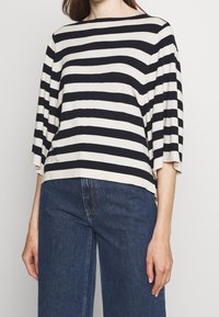 Pasiasty top w kremowym i granatowym kolorze, z szerokim dekoltem boat i rękawami trzy czwarte. Miękki materiał z luźnym krojem.