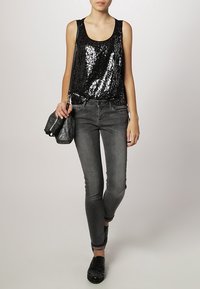 Svart paljettärmad topp med avslappnad passform, tillsammans med grå smala jeans. Outfitsen inkluderar en svart texturerad väska och svarta skor med nitar.