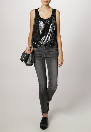 Zwarte pailletten tanktop met een ontspannen pasvorm, gecombineerd met grijze skinny jeans. De outfit bevat een zwarte gestructureerde tas en zwarte schoenen met studs.