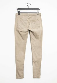 Vaqueros ajustados beige hechos de una mezcla de algodón, con una cintura de altura media, dos bolsillos traseros y un diseño limpio. Colgados de una percha negra.