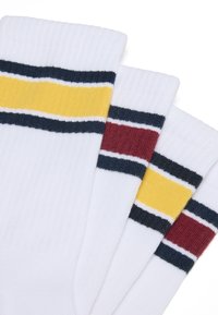 Tres pares de calcetines blancos con textura acanalada, con franjas horizontales en azul marino, amarillo y burdeos en la parte superior.