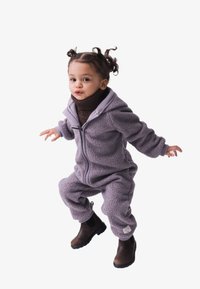 Fleece-Einteiler in helllila mit einem Frontreißverschluss, Kapuze und elastischen Bündchen. Brauner Rollkragenpullover darunter. Braune Ankle Boots.