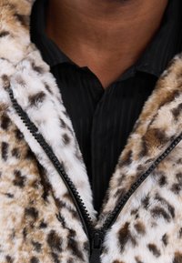 Leopardprint faux fur jakke med en sort lynlås, blød tekstur og kontrasterende hvid pelskant, båret over en sort stribet skjorte.