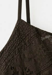 Schwarzer Spitzenstoff mit Blumenmustern und einem strukturierten Riemen, der vor einem schlichten hellen Hintergrund hängt.