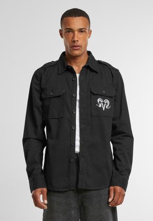 Camisa negra de botones, hecha de algodón, con dos bolsillos en el pecho y un diseño bordado de un cráneo de carnero. Mangas largas con puños abotonados.