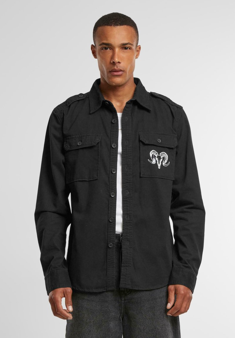 Black button-up shirt made of cotton, featuring two chest pockets and an embroidered ram skull design. Long sleeves with buttoned cuffs.