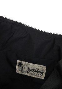 Billabong merklabel op zwarte stof met rits, met een ontwerp van een palmboom, surfer, zon en golven.