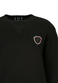 Schwarzer Strickpullover mit rundem Ausschnitt, der eine strukturierte Passe und ein gesticktes Wappenlogo in Rot, Weiß und Grün aufweist.