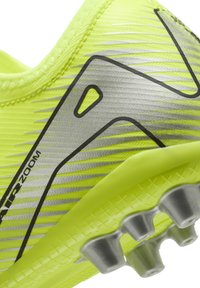 Zapatilla deportiva de color amarillo neón con un upper texturizado, acentos plateados y detalles en negro. Cuenta con una suela de goma con tacos multidireccionales.