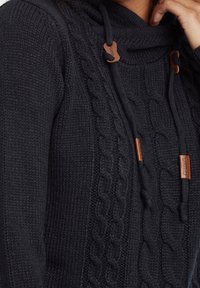 Zwarte gebreide hoodie met kabelbreipatroon en verstelbare koordjes. Beschikt over leren accenten met het merkembleem. Zachte textuur.