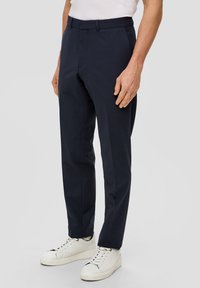 Marineblaue maßgeschneiderte Hose aus einem glatten, leichten Stoff mit flachem Bund und scharfen Falten, kombiniert mit weißen Sneakers.