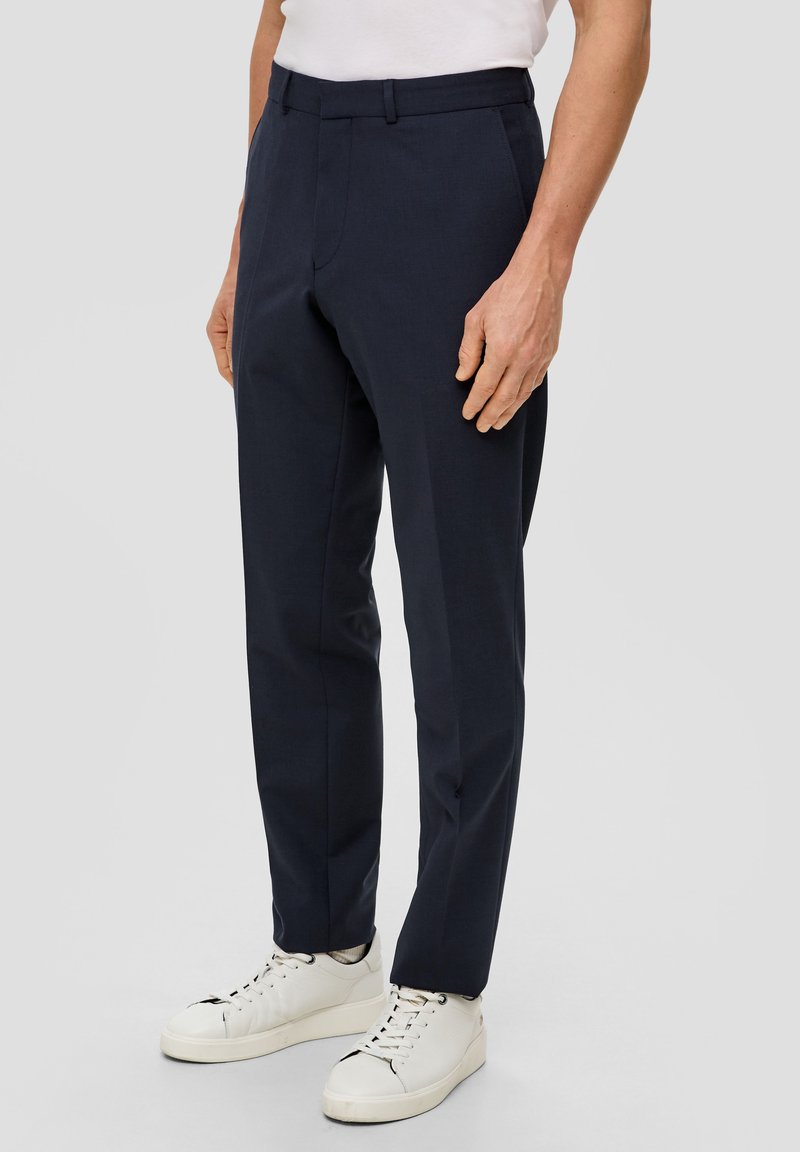 Marineblaue maßgeschneiderte Hose aus einem glatten, leichten Stoff mit flachem Bund und scharfen Falten, kombiniert mit weißen Sneakers.