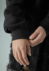 Musthave tume südamega pusa, millel on kokku volditud mansetid. Käed puhkavad kangal, tuues esile sileda tekstuuri ja luitakujunduse.