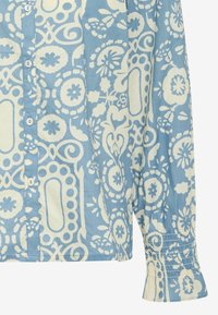 Camicia in cotone azzurro chiaro caratterizzata da un motivo floreale e geometrico bianco, chiusura con bottoni e polsini arricciati con dettaglio elastico.