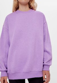 Felpa viola con scollo rotondo, spalle cadenti e maniche lunghe. Texture morbida, vestibilità rilassata e dettaglio a coste lungo l'orlo.