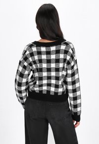 Maglione a scacchi bianco e nero con vestibilità ampia, polsini e orlo a coste neri e scollo largo. Indossato con jeans neri a vita alta.