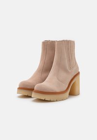 Botas de tobillo de ante beige con punta redonda, paneles laterales elásticos y un tacón grueso y transparente. Suela de goma con agarre texturizado.