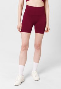 Bordeaux hoge taille shorts van rekbaar materiaal, met een gladde afwerking en een midden-dij snit, gecombineerd met witte sneakers en sokken.