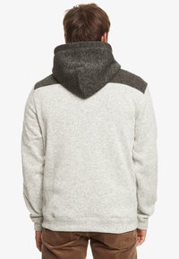 Sudadera gris con detalles en gris oscuro, tejido texturizado y capucha ajustada. Presenta un diseño tipo pullover y puños y dobladillo acanalados.