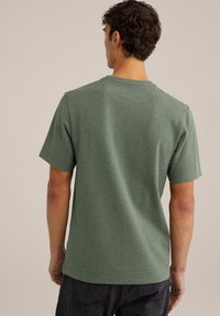 Zeleno kratko majico s kratkimi rokavi in krojnim ovratnikom, teksturirana tkanina in ravna kroja, ki prikazuje preprost in čist dizajn.