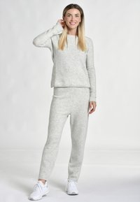 Grå fleece loungewear-set med långa ärmar, rund halsringning och slim-fit byxor. Mjuk textur, minimala sömmar, parat med vita sneakers.