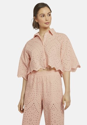 Lichtroze katoenen twee-delig kledingstuk met een cropped shirt met golfrand en oogjesdetails, en losse broek met bijpassende patronen.