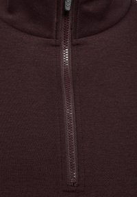 Burgundy dragkedjefleece med hög krage, som har en mjuk textur och en halv längd dragkedja på mitten. Hårdvaran är mörkt tonad.