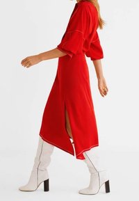 Robe midi rouge à manches courtes, avec fente sur le côté et ourlet incurvé. Associée à des bottes blanches à talons hauts avec des détails de couture noirs.