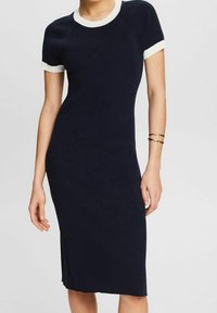 Robe en tricot côtelé bleu marine à la coupe ajustée, avec des manches courtes et un bord blanc autour de l'encolure et des manches. Comprend une fente sur le côté.