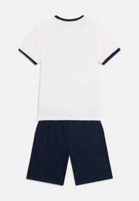 Tricou alb din bumbac cu margini bleumarin la guler și mâneci, asortat cu pantaloni scurți bleumarin. Outfit casual din două piese.