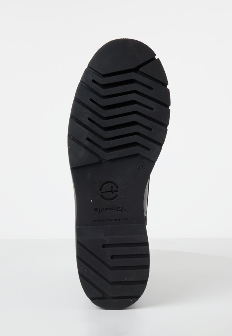 Semelle de chaussure en caoutchouc noir avec un motif de crampons prononcé, présentant un bout arrondi et un logo estampé. Design plat et robuste pour une traction et un soutien.