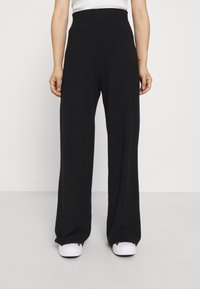 Black wide-leg pants with a soft, textured fabric, high elastic waistband, and loose fit, paired with white sneakers.