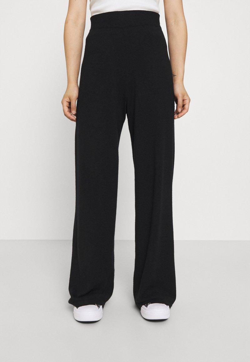 Black wide-leg pants with a soft, textured fabric, high elastic waistband, and loose fit, paired with white sneakers.