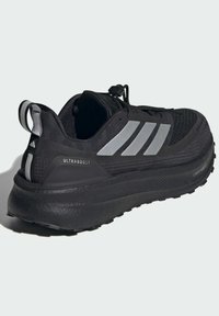 Black athletic shoe with a textured upper, silver three-stripe design, cushioned sole, and a pull tab at the heel. Features 'ULTRABOOST' branding.