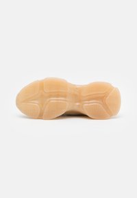 Sål af sko med et gennemsigtigt, lys tan gummimateriale med zigzag mønstre og strukturerede riller for greb.