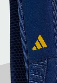 Blå atletisk ryggsäck med en texturerad tyg och mesh sidoficka, med en gul Adidas logotriangel på framsidan.