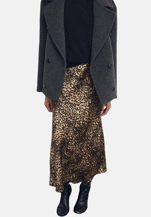 Falda maxi de satén con estampado de leopardo combinada con un abrigo de lana oscuro de doble botonadura y botas negras en los tobillos.