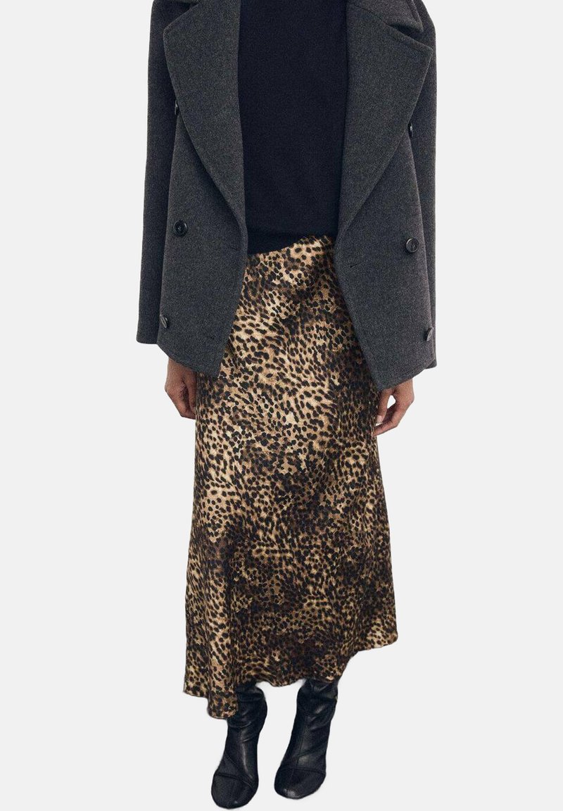 Falda maxi de satén con estampado de leopardo combinada con un abrigo de lana oscuro de doble botonadura y botas negras en los tobillos.