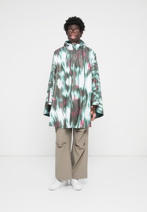 Patterned poncho in shades of teal, white, and pink, featuring a hood and wide sleeves. Paired with beige wide-leg pants and white shoes.